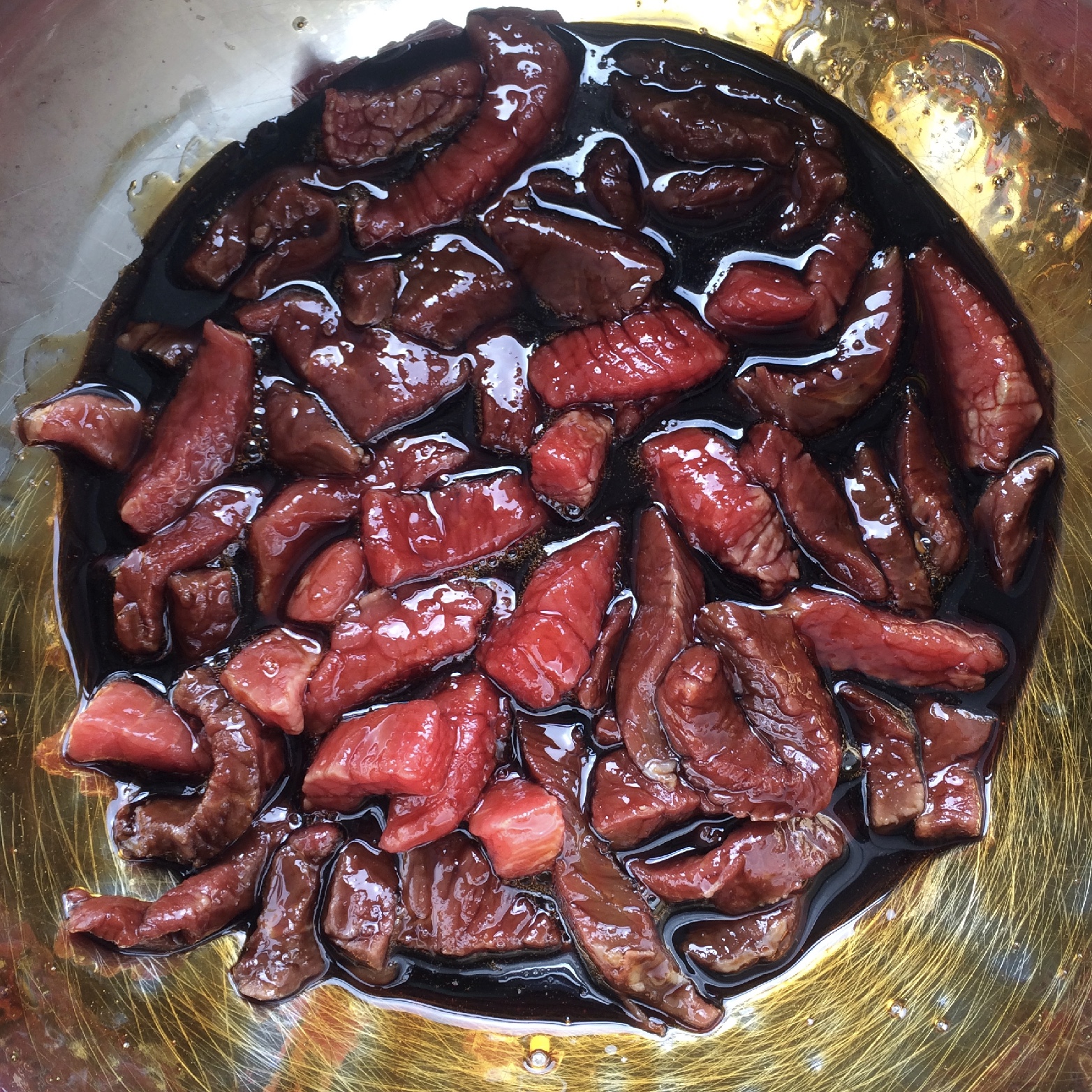 Thin strips of diced lean beef marinading in a bowl of liquid spices
